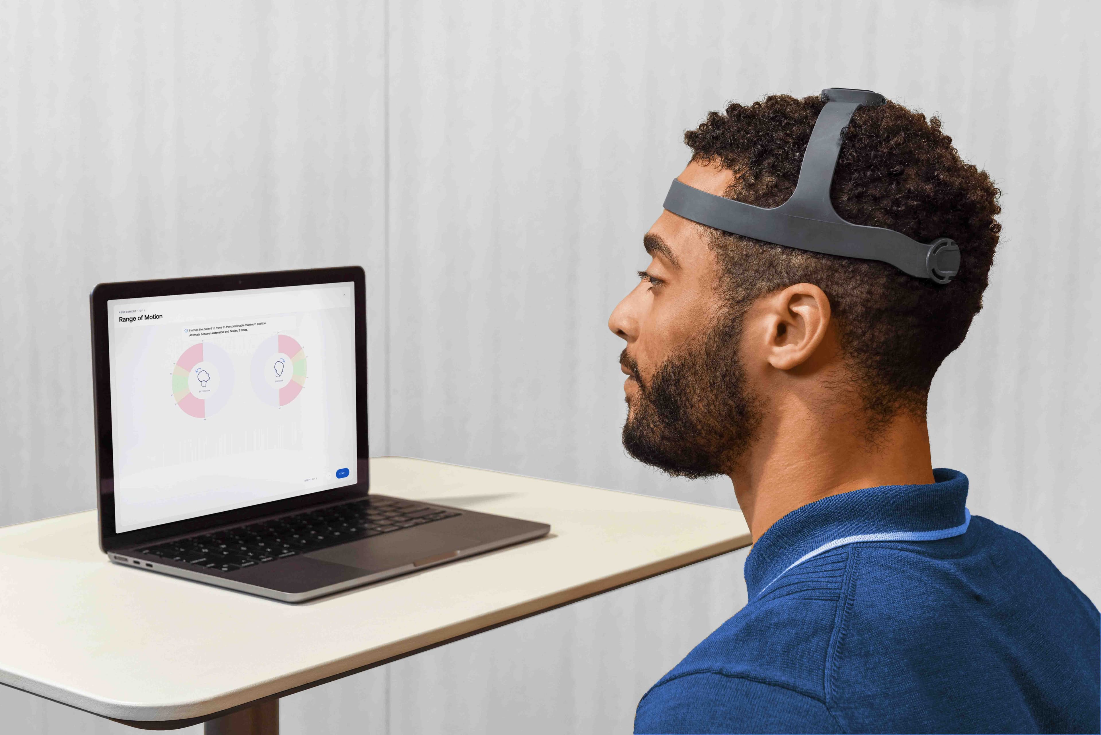 A man wearing the NeckCare device sits at a table, looking at a laptop screen that displays neck range of motion assessment graphs.